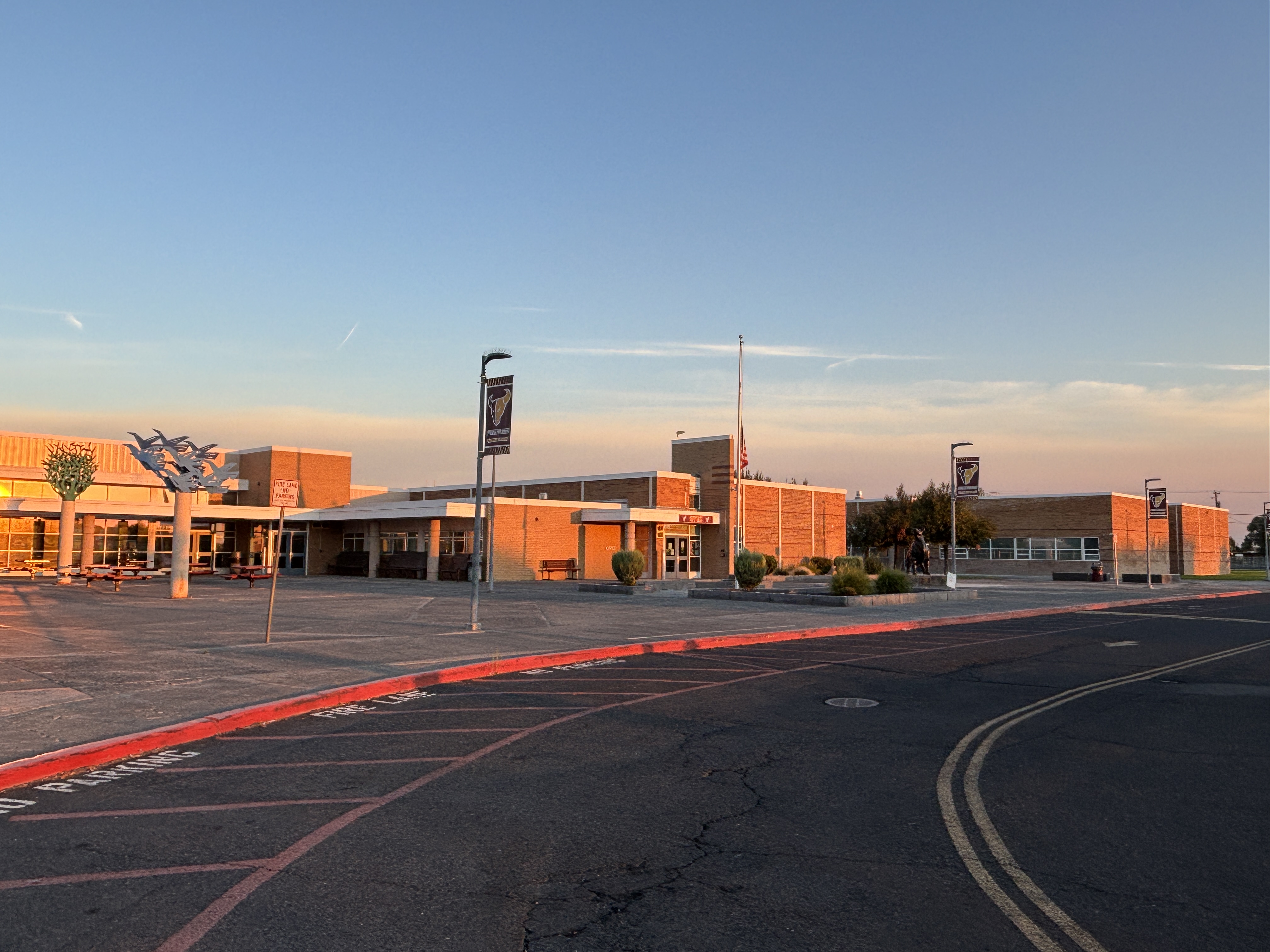 A modern school building with brick facades and large windows under a clear sky at sunset.